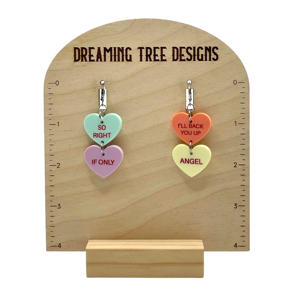 a couple of heart shaped earrings hanging from a wooden stand